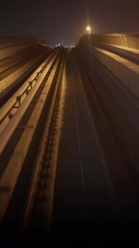 Metro train POV descends along an elevated railway track toward bright city lights at night