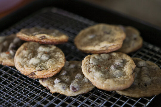 Freshly baked chocolate chip cookies cool on wire rack, golden brown edges and soft centers evoke warmth and comfort of homemade treats.