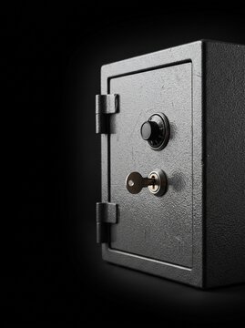Close up of a gray metal safe with a combination lock and a key inserted into the lock against a dark background
