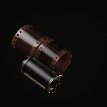 Vintage 35mm film roll and canister on a black background, representing analog photography and nostalgia