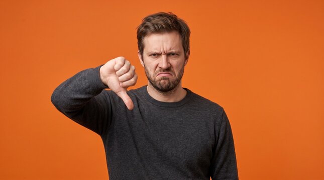 Displeased man giving a thumbs down gesture on orange background