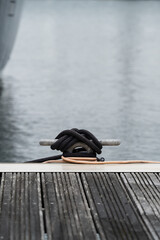 Black mooring rope tied around dock cleat on wooden marina pontoon with water copy space © Jane Allan