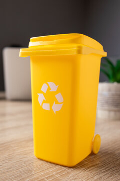 Yellow mini recycling bin on a wooden desk with a white recycling symbol. Representing sustainability. Environmental awareness. Waste management