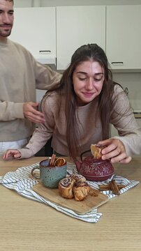 Man stealing a cinnamon roll from his girlfriend at a cozy breakfast table, playful couple moment