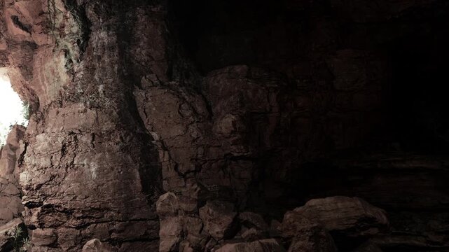 In a dark cave, shadowy rock formations rise majestically. Subtle light peeks through a small opening, illuminating the rugged textures and creating a sense of enchantment and wonder.