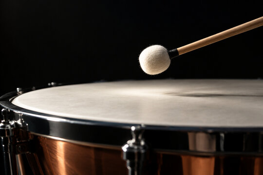 Drumstick poised just above the skin of a timpani drum.