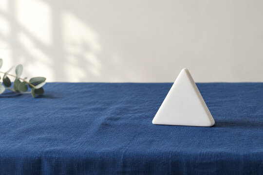 Single white equilateral triangle object on deep blue linen, calm still life for editorial concept