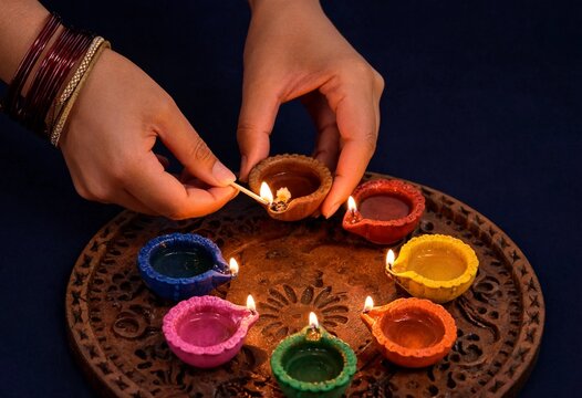 Hands lighting colorful Diwali oil lamps