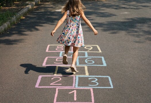 Girl playing hopscotch outdoors on pavement