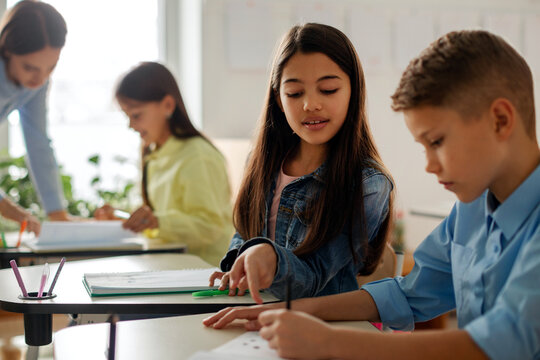 Elementary school girl explaining something to male classmate at desk