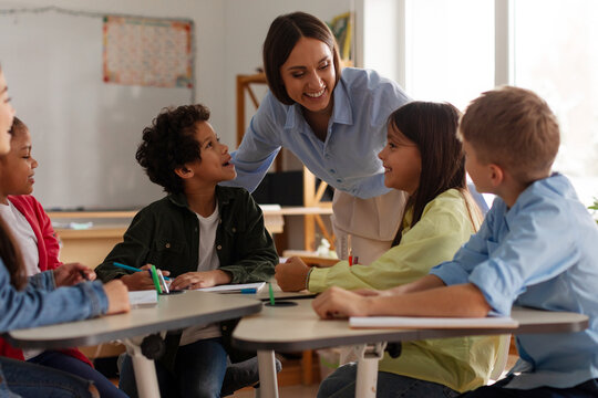 Female teacher interacting with group of primary school students during classroom activity