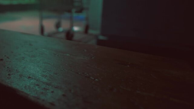 A weathered wooden table stands in a dimly lit room, highlighted by an inviting green glow. Shadows dance across the floor, creating a peaceful ambiance that invites relaxation.