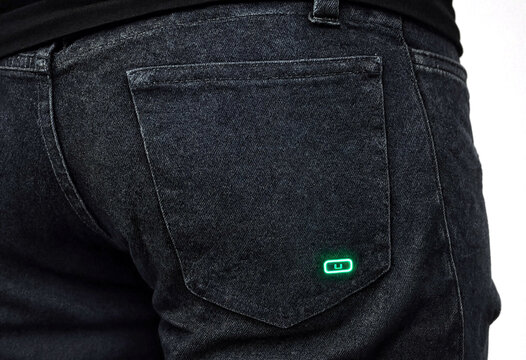 Closeup shot of the back pocket of dark wash denim jeans featuring a small glowing neon green square logo on the fabric