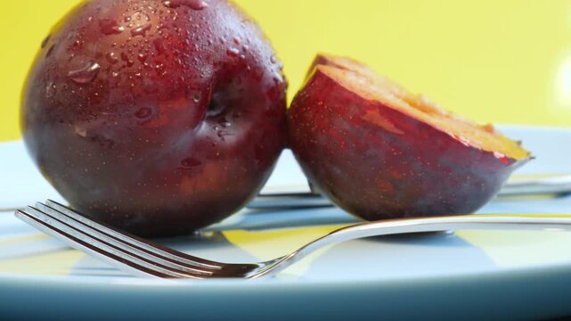 Ripe, juicy plums with fork and knife on a blue plate. Juicy plum cut in a half. Fruits and time of harvesting. Juicy plums sprinkled with water close up.	
