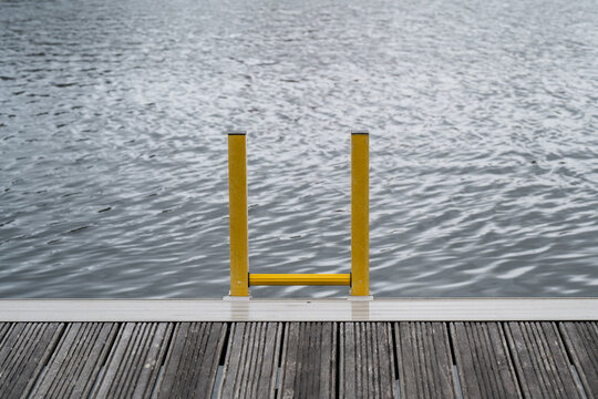Yellow marina ladder on wooden dock leading into rippling water with simple symmetrical composition