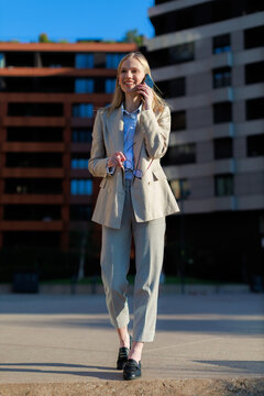 happy businesswoman walking and talking on smartphone in city