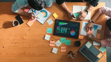 Obraz premium Top aerial view of diverse team writing colorful sticky notes to brainstorm marketing idea while looking at financial chart. Multicultural smart business people taking a note about plan. Convocation.