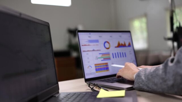 A business woman analyzing sales performance data and financial charts on a laptop computer in a modern office.