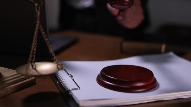 A judge's gavel striking down on a block next to a scale of justice and legal documents in a courtroom or law office setting.