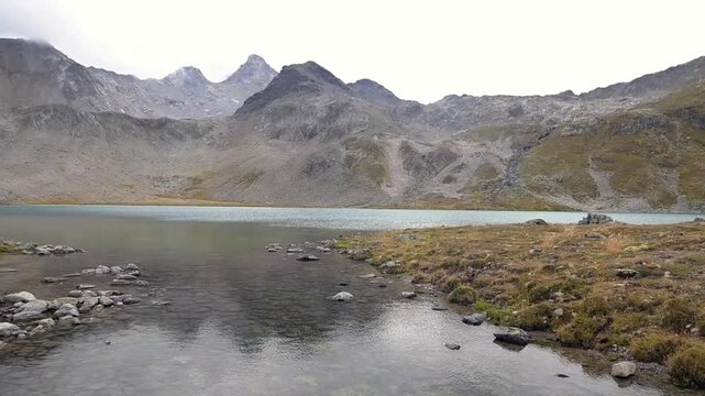 Calm mountain lake bordered by rocky alpine slopes and autumn tundra in the Swiss Alps.