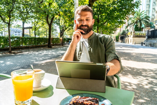 Man working on tablet outdoors enjoying coffee and breakfast
