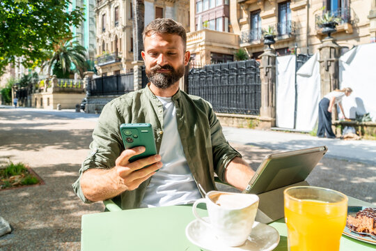 Man using smartphone and tablet at cafe terrace