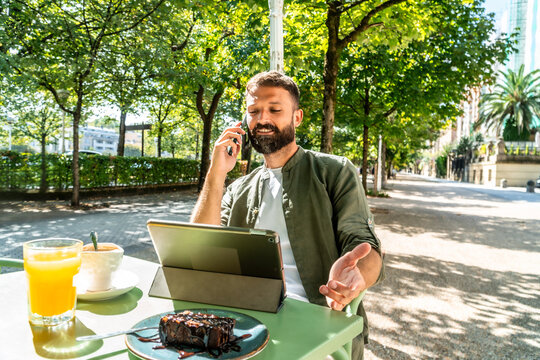 Man working remotely, talking on phone outdoors cafe