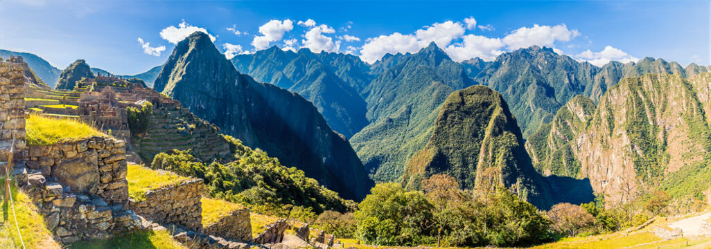 A panorama view of the historic sanctuary of Machu Picchu in Peru, featuring ancient Incan stone ruins and terracing set against the dramatic backdrop of the Andean mountains in the dry season