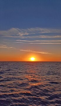 Vertical view of a brilliant golden sunset over open ocean with glowing sun reflections on waves
