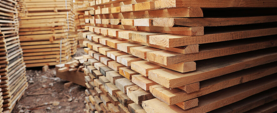 Stacks of lumber outdoors, displaying natural grain of wood. Sawmill warehouse. Industrial woodworking. Narrow banner