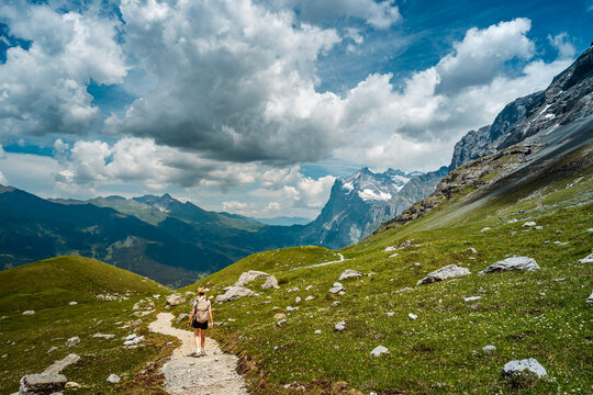 Woman with a backpack hiking a mountain trail toward the Wetterhorn under dramatic clouds