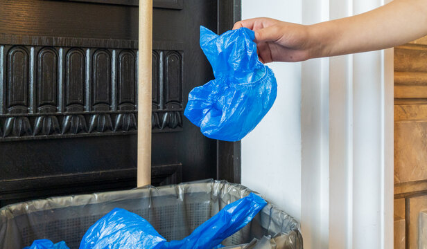 Hand Dropping Used Blue Shoe Cover into Waste Bin. Medical Plastic Waste Concept