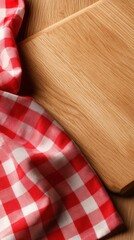 Obraz premium Red and white checkered picnic cloth partially covering a smooth wooden cutting board on a wooden surface for rustic kitchen or outdoor meal setting background