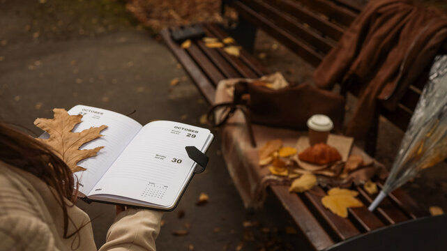 Autumnal park scene with open planner, croissant, and coffee on a bench