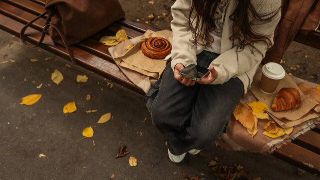 Person sitting on park bench with coffee and pastry enjoying autumn weather