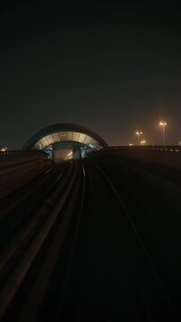 Train POV moves along elevated railway tracks through an arched metro station, then continues toward illuminated urban lights at night