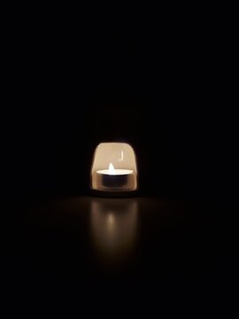 Burning candle inside white ceramic aroma lamp on black background