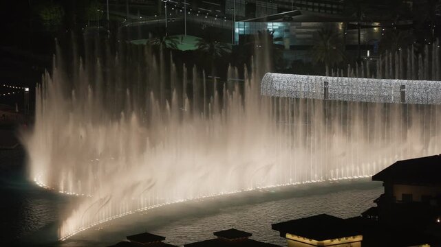 Dubai Fountain water jets rise and fall in slow motion, forming a glowing curtain across Burj Lake at night