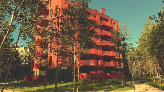 Modern apartment building surrounded by green trees and walking path in eca neighbourhood. Multifamily residential real estate in green infrastructure in nature. New apartment building in red facade.