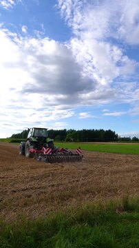 Modern green tractor with agricultural cultivator working in a harvested field, farm machinery preparing soil under a blue sky, rural agriculture and farming scene