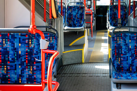 Interior of empty public bus with colorful patterned seats and bright red handrails. The aisle is clear, leading to the driver's area.