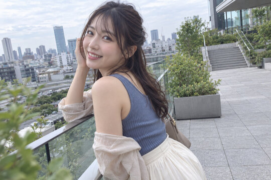 屋上テラスのガラス手すりで振り返り笑う青いトップス姿の女性
