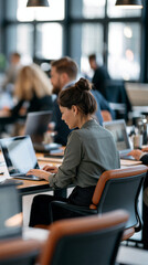 Fototapeta premium Rear view of a young couple sitting at desks with laptops preparing for an online meeting, bright open plan office background with large windows, remote meeting preparation,