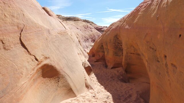 Camera movement walking through a narrow sandstone slot canyon with red-orange walls and a sandy bottom under a clear blue sky, showing the beautiful rock formations of valley of fire, nevada