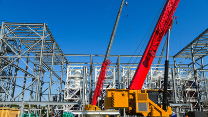 A yellow construction crane with a long red boom is used for lifting and installing metal structures. © SGr