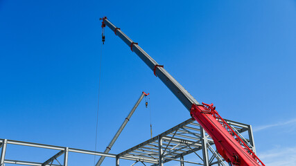 A yellow construction crane with a long red boom is used for lifting and installing metal structures. © SGr