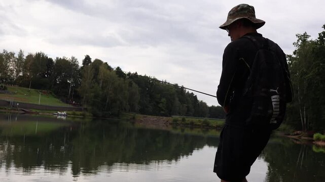 Young fisherman casting rod on a calm lake shore, targeting asp (Aspius aspius). Active outdoor lifestyle and sportfishing.