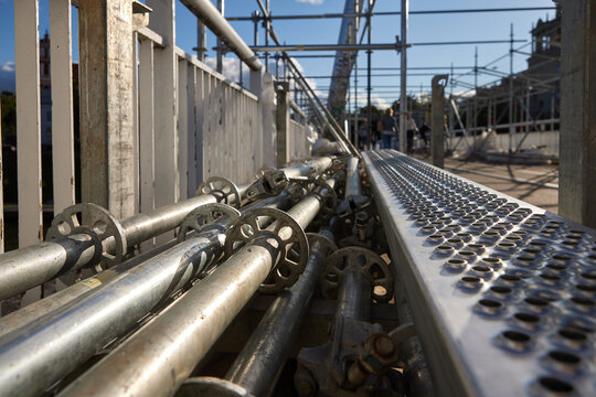 Construction scaffolding, metal pipes, temporary access platform and industrial structure at a bridge renovation site. Galvanized steel scaffold tubes, perforated walkway with workers