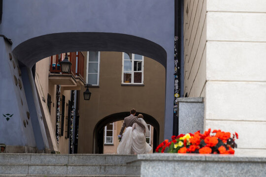 Warsaw, Poland, 5 September 2026,  Bride and groom walking hand in hand away through arched passage on Kanonia Street