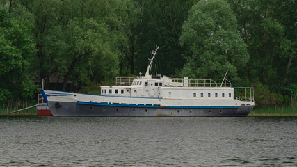 Fototapeta premium White passenger motor ship moored near lush green forested riverbank